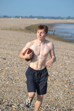 Genç bir çocuk, sıcak bir yaz gününde kumsalda elinde Amerikan futbolu topuyla kameraya doğru koşuyor.