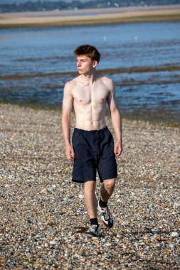 Teenage boy walking towards the camera, along a beach on warm summer's day