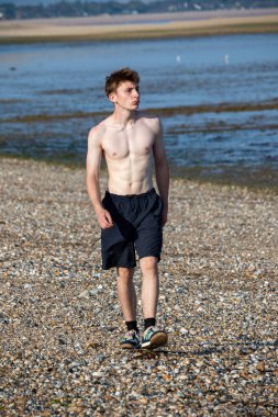 Teenage boy walking towards the camera, along a beach on warm summer's day