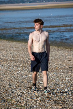 Teenage boy walking towards the camera, along a beach on warm summer's day