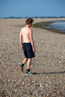 Teenage boy walking away from the camera, along a beach on warm summer's da