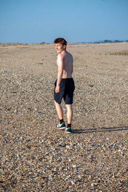 Teenage boy turning  towards the camera, along a beach on warm summer's da