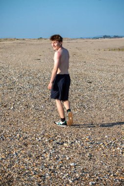 Teenage boy turning  towards the camera, along a beach on warm summer's da