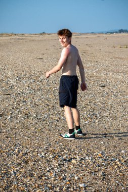 Teenage boy turning  towards the camera, along a beach on warm summer's da