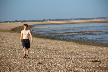 Teenage boy walking towards the camera, along a beach on warm summer's day, landscape shot