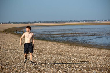 Teenage boy walking towards the camera, along a beach on warm summer's day, landscape shot