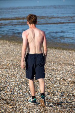 Teenage boy walking away from the camera, along a beach on warm summer's da