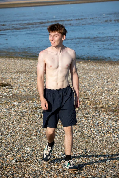 Teenage boy walking towards the camera, along a beach on warm summer's day