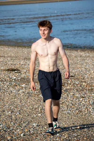 Teenage boy walking towards the camera, along a beach on warm summer's day