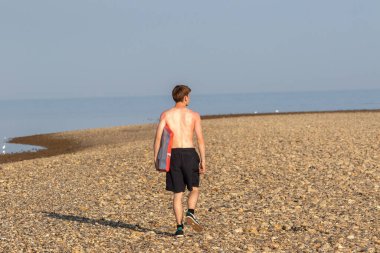 Teenage Boy Walking Along a Beach, carrying a body board on a warm summer's day