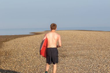 Teenage Boy Walking Along a Beach, carrying a body board on a warm summer's day