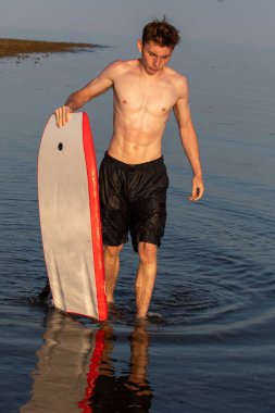 Teenage boy in the sea with a boy board on a warm summer's evening