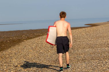 Teenage Boy Walking Along a Beach, carrying a body board on a warm summer's day