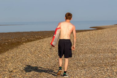 Teenage Boy Walking Along a Beach, carrying a body board on a warm summer's day
