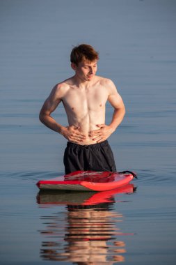 Teenage boy standing in the sea, with a body board, on a warm summer's evening
