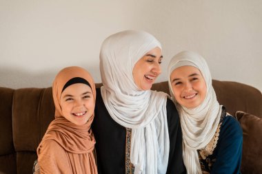 Evde mutlu bir Müslüman ailenin portresi, tesettürlü bir anne ve iki kızı kameraya bakıyor ve Anneler Günü 'nde gülümsüyor. Yüksek kalite fotoğraf
