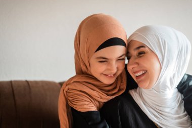 Evde mutlu bir Müslüman aile, bir anne ve kız kanepede sevgiyle sarılıyor, anneler gününde şefkat göstermek için birlikte gülüyor ve oynuyorlar. Yüksek kalite fotoğraf
