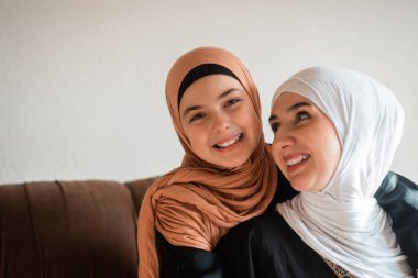 Evde mutlu bir Müslüman aile, bir anne ve kız kanepede sevgiyle sarılıyor, anneler gününde şefkat göstermek için birlikte gülüyor ve oynuyorlar. Yüksek kalite fotoğraf