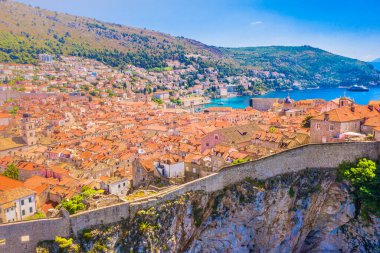Aerial scenic view of Dubrovnik old town showing ancient city walls rising above the rooftops, blue Adriatic sea, historic architecture and marble Mediterranean cityscape