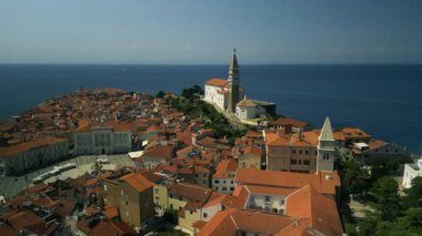 Dar caddelerde kırmızı çatıları olan eski evlerin üzerinde kilise taşı çan kulesi yükseliyor. Tarihsel Avrupa kentini çevreleyen güneş ışığı altında deniz ufku parıldıyor