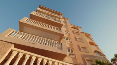 Şehir manzarası alçak açılı, mavi gökyüzünün altında köşe balkonları olan bir otel binası. Yerleşim yerleri turistleri şehre çekiyor. Şehir mimarisi