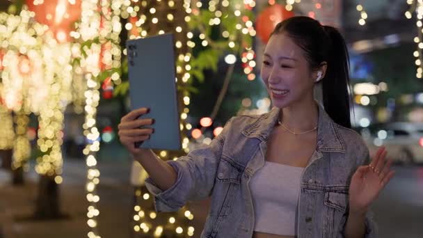 Portrait of Asian woman talks on video call via digital tablet in night megapolis. Happy Korean lady waves hand Hello to friend online on downtown street slow motion. Internet chat Portrait of Asian woman talks on video call via digital tablet in night megapolis. Happy Korean lady waves hand Hello to friend online on downtown street slow motion. Internet chat