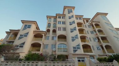 Alçak açılı çekimde bej ön cepheli ve kemerli loggiaları olan muhteşem bir otel. Akdeniz tarzı çok katlı bina modern şehirde lüks daireler satın almak için davet edildi