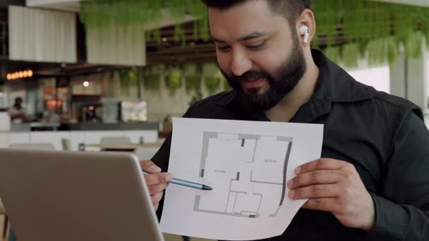 Portrait of happy Indian architect shows renovations on flat floor plan on video call in office. South Asian engineer designer shares project of home improvement via laptop indoors Portrait of happy Indian architect shows renovations on flat floor plan on video call in office. South Asian engineer designer shares project of home improvement via laptop indoors