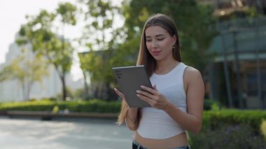 Kahverengi saçlı güzel bir kadının portresi şehir parkında dijital tablet kullanıyor. Sakin bir kadın, sosyal medyayı yaz bahçesinde taşınabilir bilgisayarla tarıyor. İnternet ağı