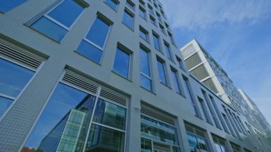 Camdan pencereleri ve mavi gökyüzü altında temiz çağdaş mimarisi olan modern bir ofis binasının düşük açılı görüntüsü. Ticari, teknolojik ve kentsel kavramlar için şirket gayrimenkulleri.