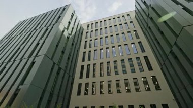 Soldan sağa doğru yavaş yatay panelli statik manzara, şehir ortamında modern ofis binalarının temiz cepheli, dikey pencereli ve çağdaş kurumsal mimari yapılarını gösteriyor.