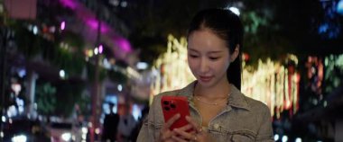 Genç Asyalı kadın portresi akıllı telefon tutar ve gece şehir merkezindeki anamorfik lenslere bakar. Güzel Çinli kadın cep telefonunu şehir caddesinde duruyor gibi kullanıyor.