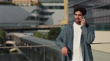 Genç İspanyol 'un portresi akıllı telefondan konuşuyor ve yavaş çekimde cam korkuluklara yaslanıyor. Latin Amerikalı bir adam cep telefonuyla arıyor.