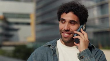 Sakallı İspanyol adamın portresi şehir merkezindeki ofis binalarına karşı akıllı telefondan konuşuyor. Kot gömlekli genç Latin Amerikalı erkek şehirdeki cep telefonuyla konuşuyor.