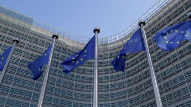 BRÜKSEL, BELGIUM - 27 Eylül 2025: Berlaymont 'taki mavi gökyüzü alçak açılı çekimin altında rüzgarda rüzgarda sallanan yıldız daireli AB bayrakları. Avrupa Komisyonu idari daireleri