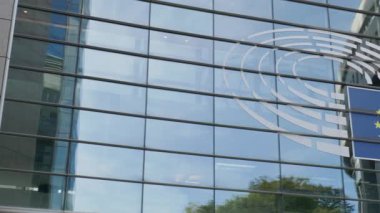 BRÜKSEL, BELGIUM - 27 Eylül 2025: Avrupa Parlamentosu, şehir merkezindeki mavi bayrak ve yuvarlak logoyu yansıtan cam cephe. Uluslararası birlik kompleksi