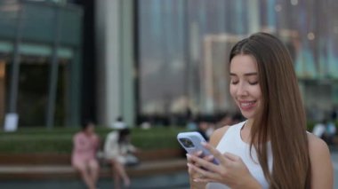 Güzel bir kadının portresi akıllı telefona bakar ve şehir merkezinde yürür. Beyaz tişörtlü kahverengi saçlı kadın sokakta yürürken internette cep telefonuyla konuşuyor.