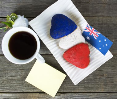 Heart shaped cookies red, white, blue.  cup of coffee (tea), Australia flag - decoration on old wooden table. notebook Happy Australia Day and koala. Sunny morning. Toned colored