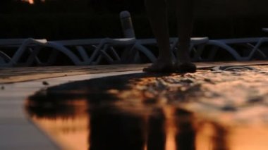 Gün batımında çıplak ayaklı adam yüzme havuzunun yanında yürür. Havuzda dalgalar. Havuzun dalgaları ayaklarına vurdu - 4K