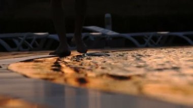 Gün batımında çıplak ayaklı adam yüzme havuzunun yanında yürür. Havuzda dalgalar. Havuzun dalgaları ayaklarına vurdu - 4K