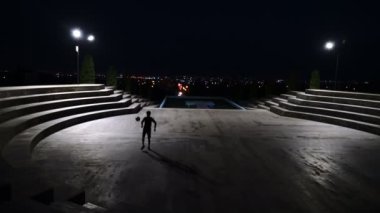 Geceleri şehrin arka planında futbol oynayan bir adamın silüeti - 4K