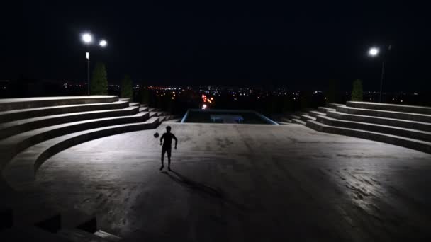 街の背景を背景に夜サッカーをする男のシルエット — ストック動画
