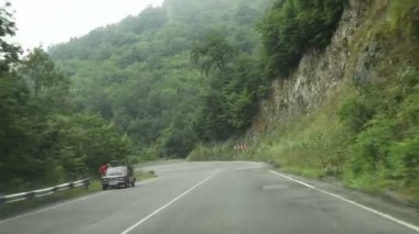 Araba, dağlık bir bölgenin ortasında asfaltlı düz bir yolda ilerliyor.