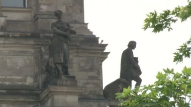 Berlin 'deki Reichstag binasında heykeller, taş heykeller ve levhalar, binada Alman bayrakları, çatıda cam kubbe.