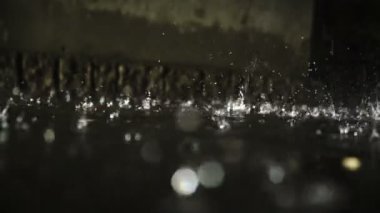 Yağmur damlaları karanlıkta birikintiyi vurur. 