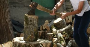 Ağaç kütüğündeki bir çocuk beceriksizce baltayla odun kesiyor. Ocağı yakmak için odun hazırlıyorum. Sıcak, yumuşak bir ışık. 4K.