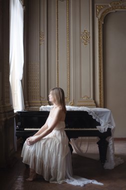 Güzel kız beyaz vintage elbise ve bir piyano zengin iç.