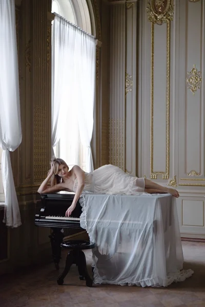 白いヴィンテージのドレスと豊富なインテリア ピアノで美しい少女. — ストック写真