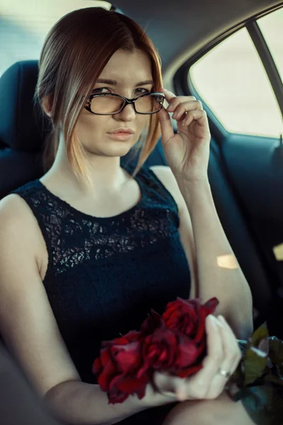 Mädchen mit Brille auf dem Rücksitz hält Rosen in der Hand. — Stockfoto