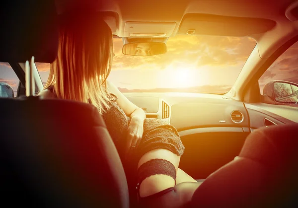 Junges Mädchen in schwarzen Strümpfen wedelt mit Sonnenuntergang im Auto. — Stockfoto